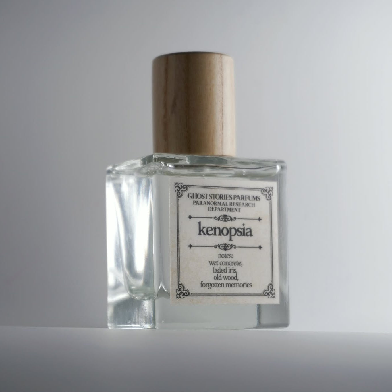 Perfume bottle labeled 'kenopsia' with a wooden cap on a gray background