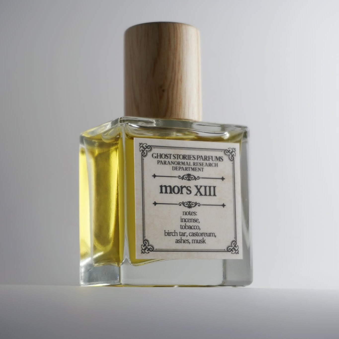Perfume bottle labeled 'mors XIII' with a wooden cap on a light gray background