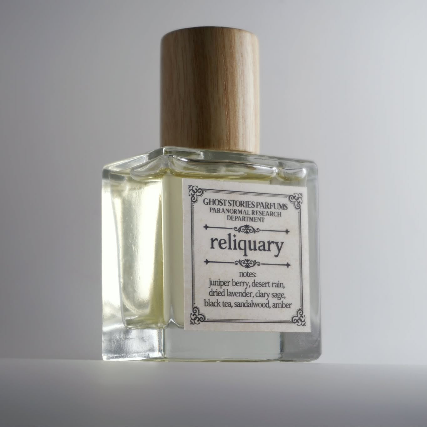 Perfume bottle labeled 'reliquary' with a wooden cap on a gray background